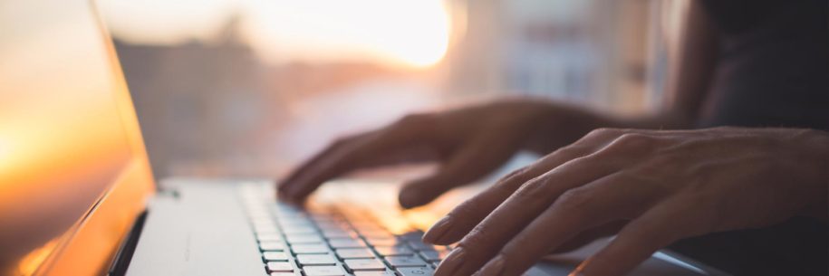 Woman's hands on a laptop keyboard as the sun rises.